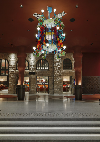 Foto av inngangshall i nye hjorten teater, fargerik lysekrone og røde roner på vegger.