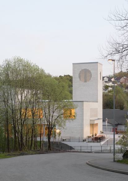 Foto av en vei som leder ned til en kirke i hvit teglstein, trær i forgrunnen.
