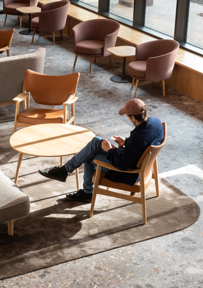 Interiørfoto av Tønsberg Tinghus som viser en mann som sitter i venteareal for publikum. Gulvet er i grå terazzofliser, møblene er i tre, skinn og stoff i duse farger. 